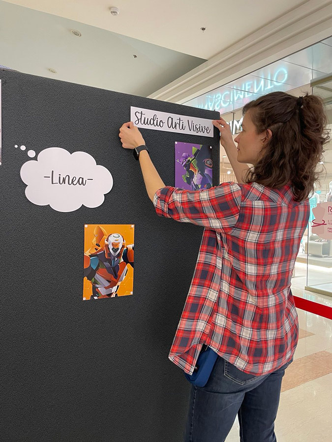 Ragazza allestisce una mostra su una parte espositiva nera appendendo dei disegni colorati